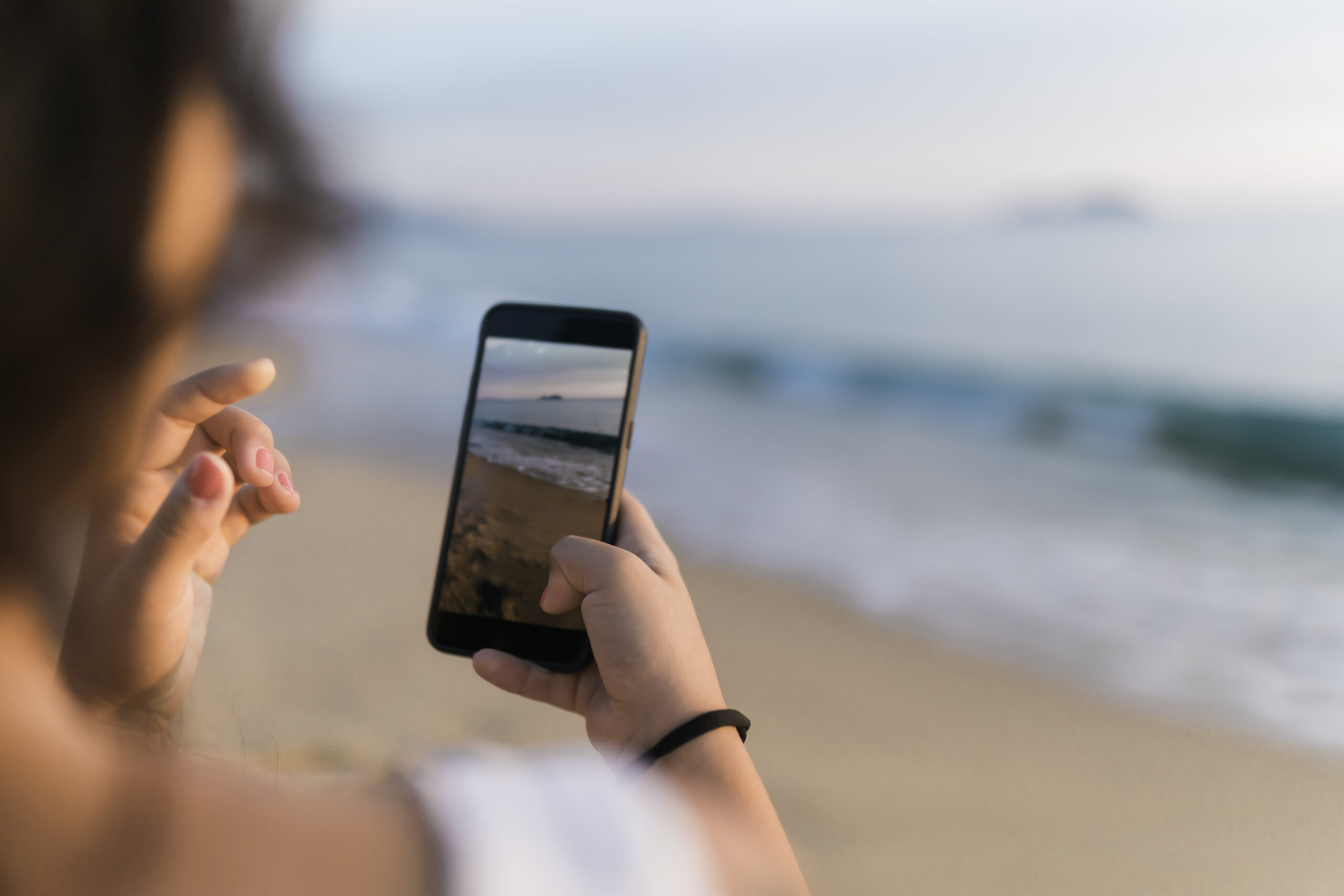 Person taking beach photos on phone at sunset