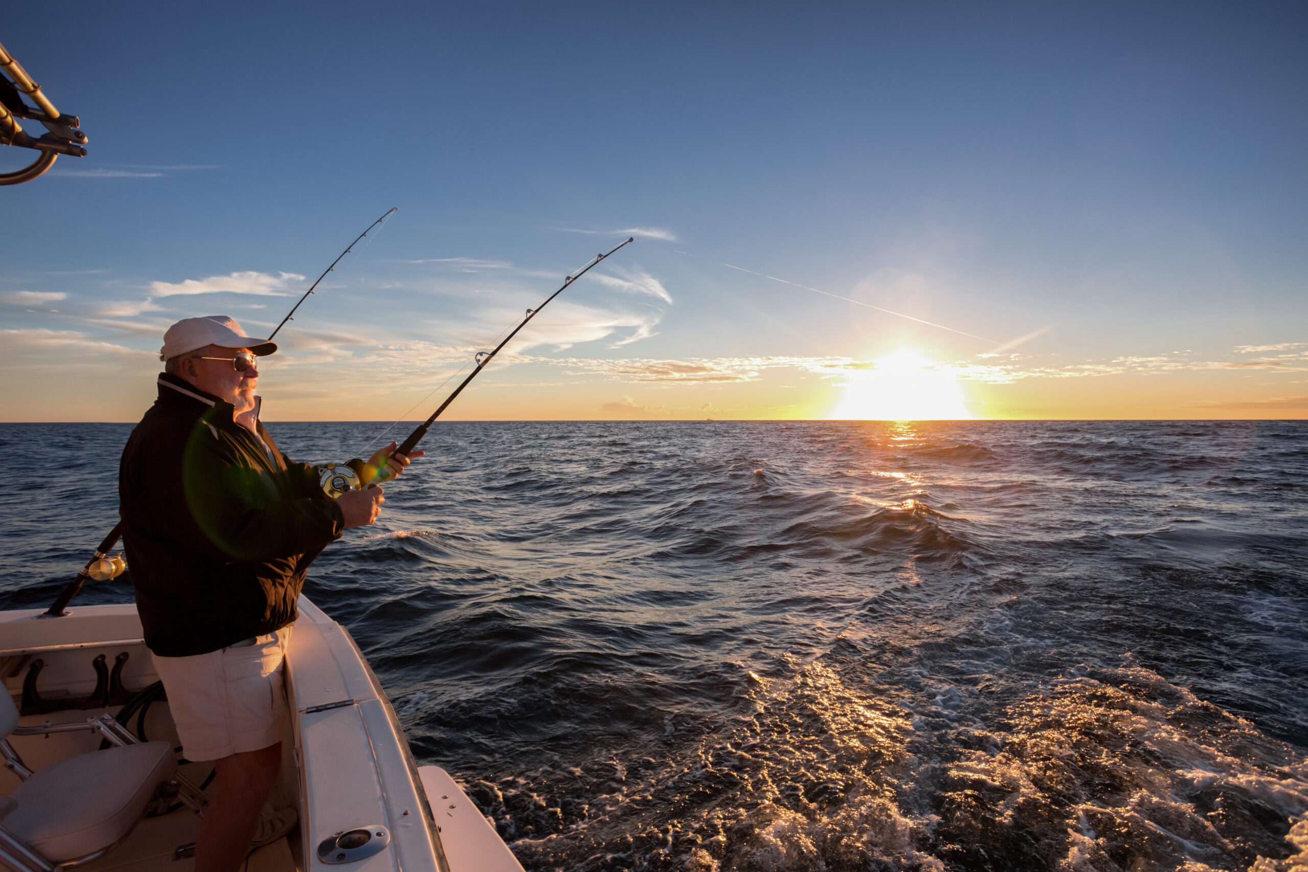 Elderly man fishing from beach pier at sunset